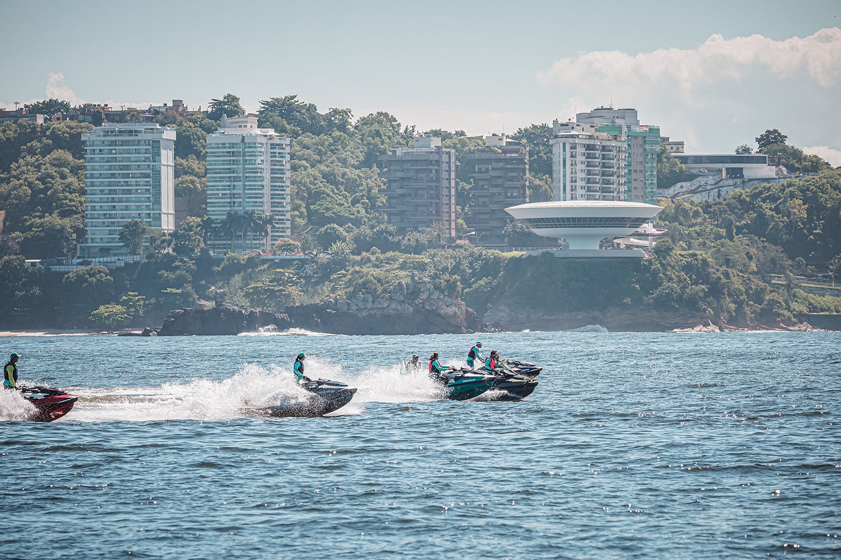 Pilotos alinhados acelerando em perspectiva com paisagem de montanhas e árvores ao fundo.
