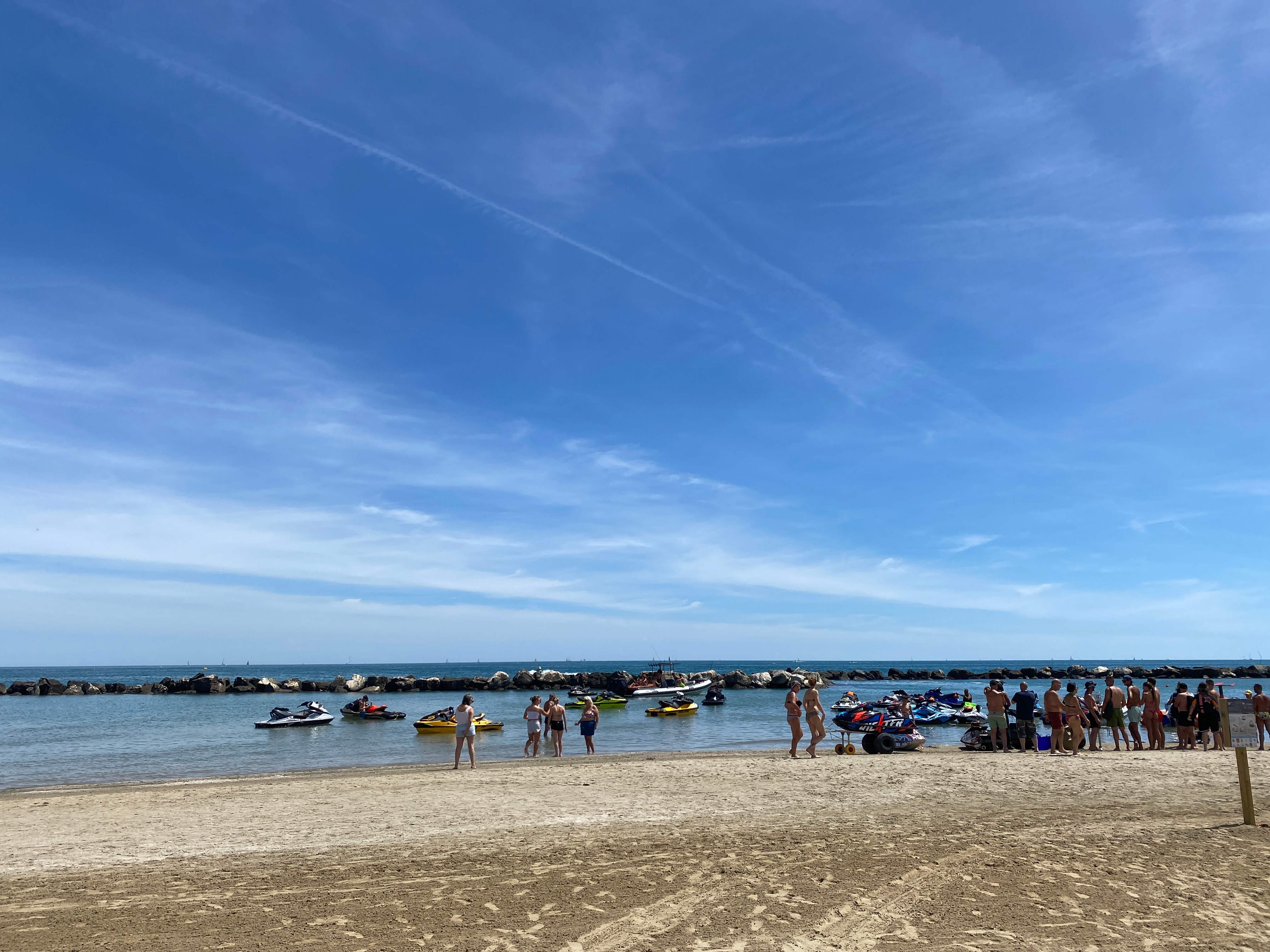 Persone che passeggiano sulla spiaggia accanto a diverse moto d'acqua Sea-Doo ormeggiate in acqua