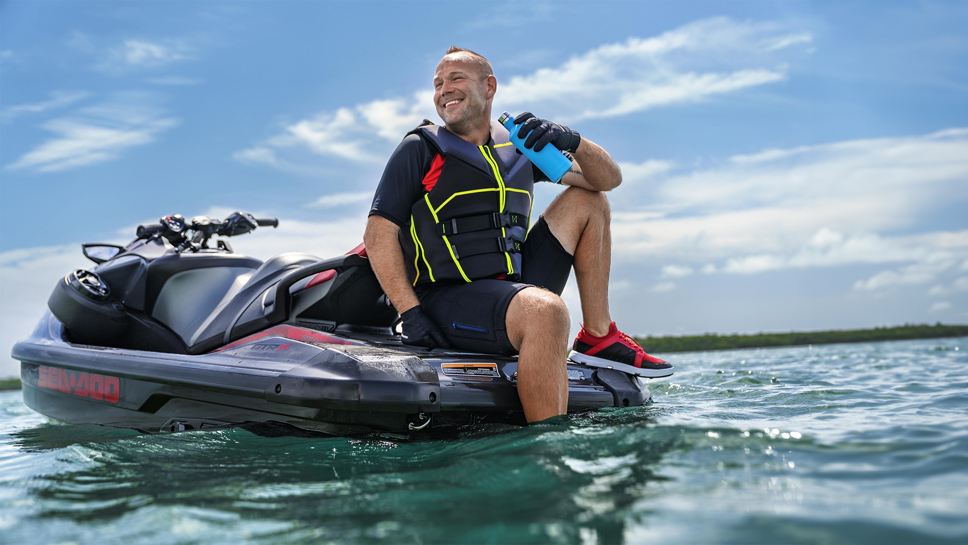 Homem segurando uma garrafinha, sorrindo sentado em cima da Sea-Doo GTR-X 300