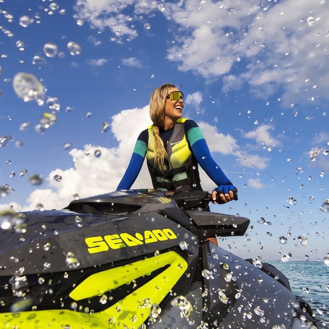 A woman wearing Sea-Doo gear on her personal watercraft on a sunny day