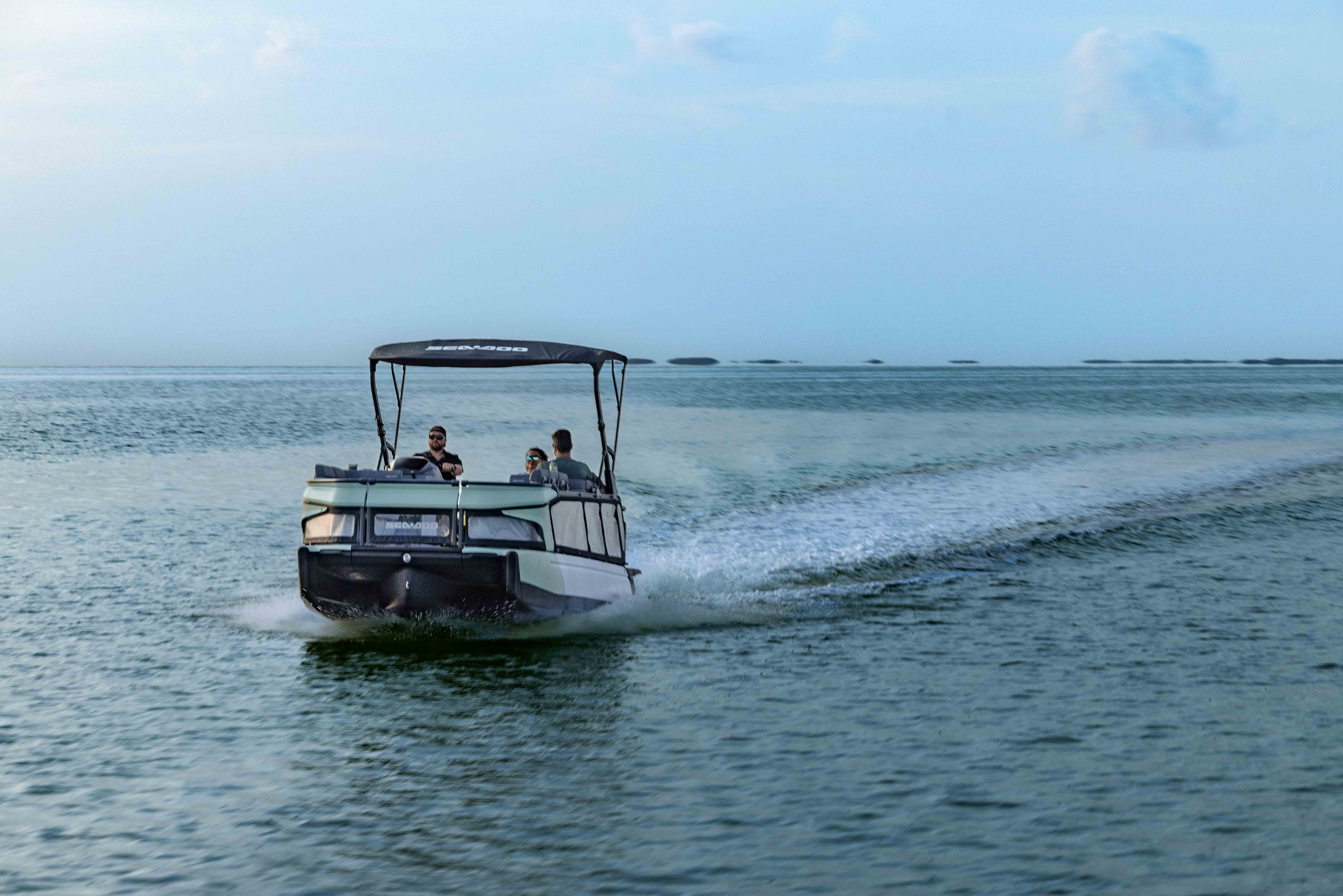 A family aboard a 2026 Sea-Doo Switch Cruise pontoon boat on calm water
