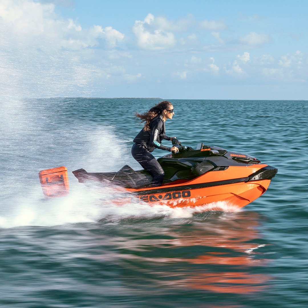 A woman riding a 2027 Sea-Doo RXT-X personal watercraft at full speed