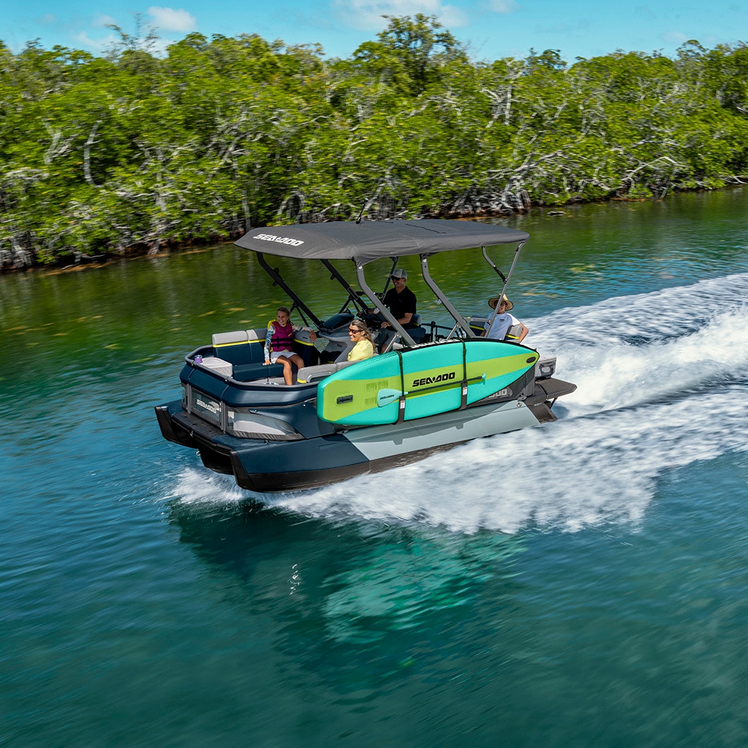 A family on a 2027 Sea-Doo Switch pontoon boat near the shore of a lake 