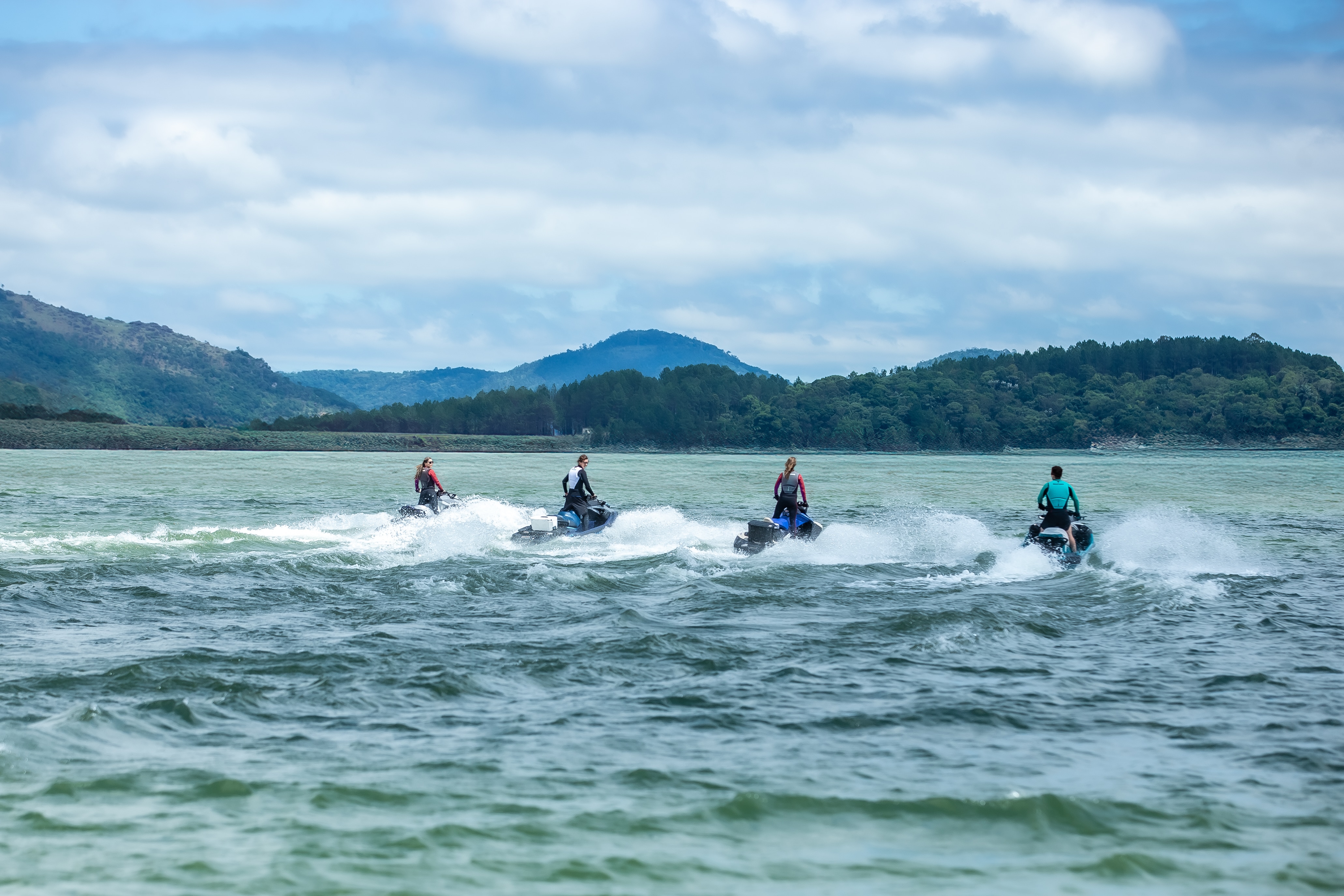 Grupo de pessoas a bordo de modelos Sea-Doo em movimento na água, de costas para a foto