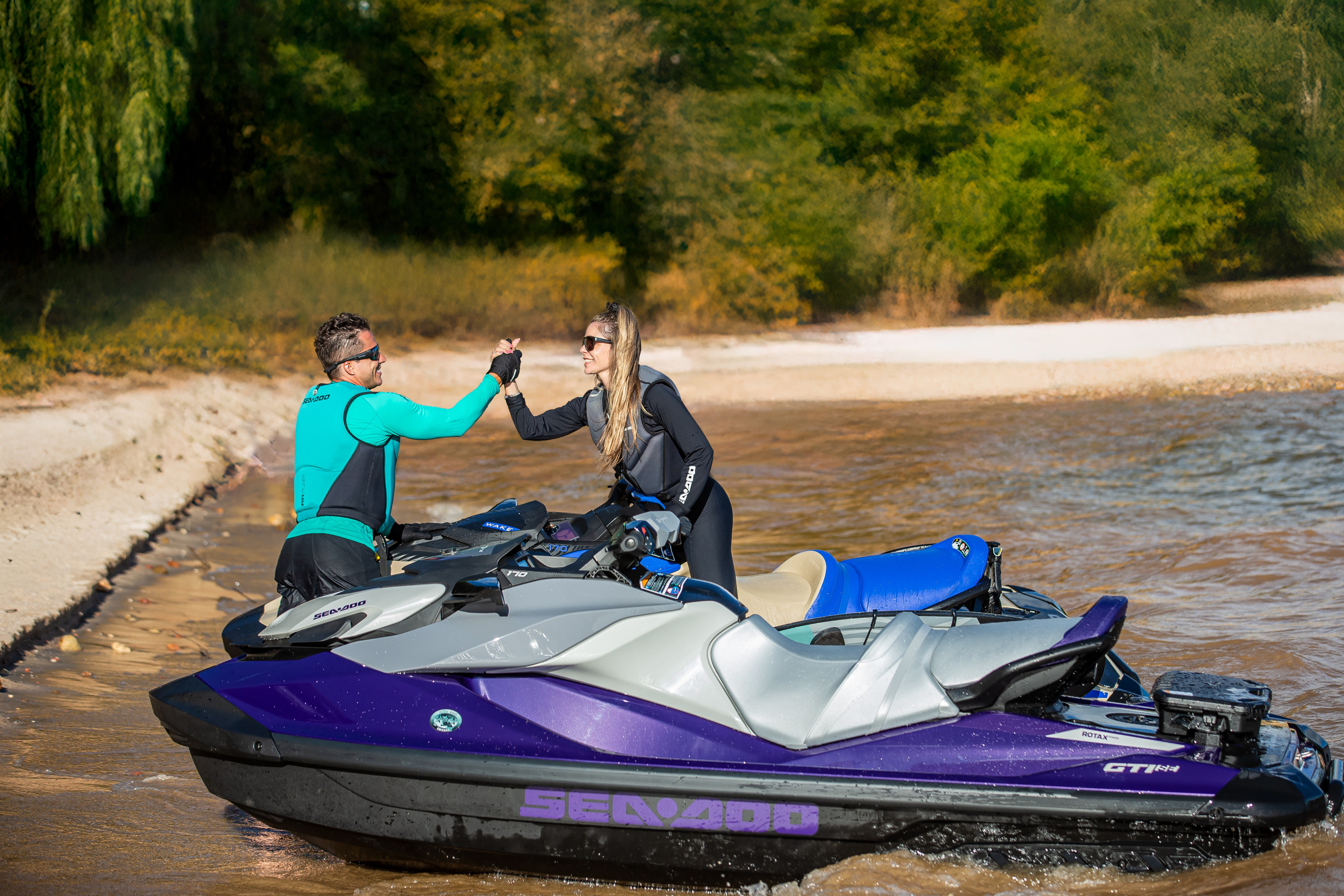 Dois pilotos parados e se cumprimentando próximos aos modelos Sea-Doo estacionados em uma orla