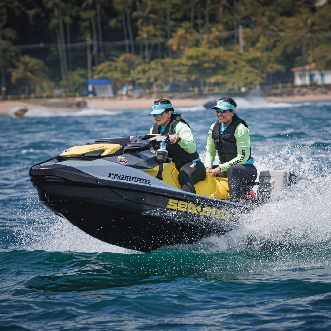 Mulher pilotando moto aquática com outra mulher na garupa.