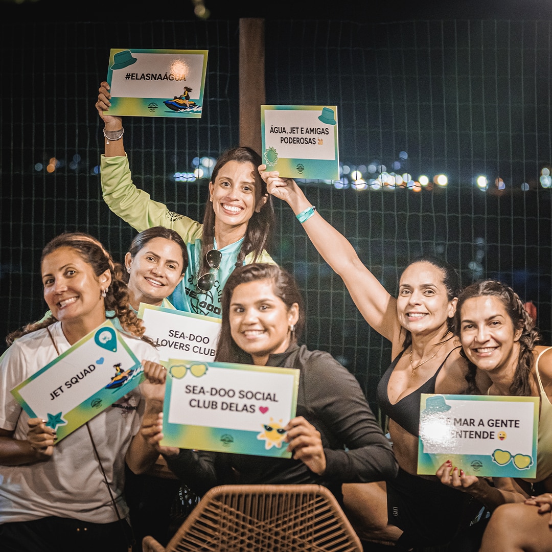 Grupo de mulheres segurando placas com frases diversas enquanto posam para a foto.