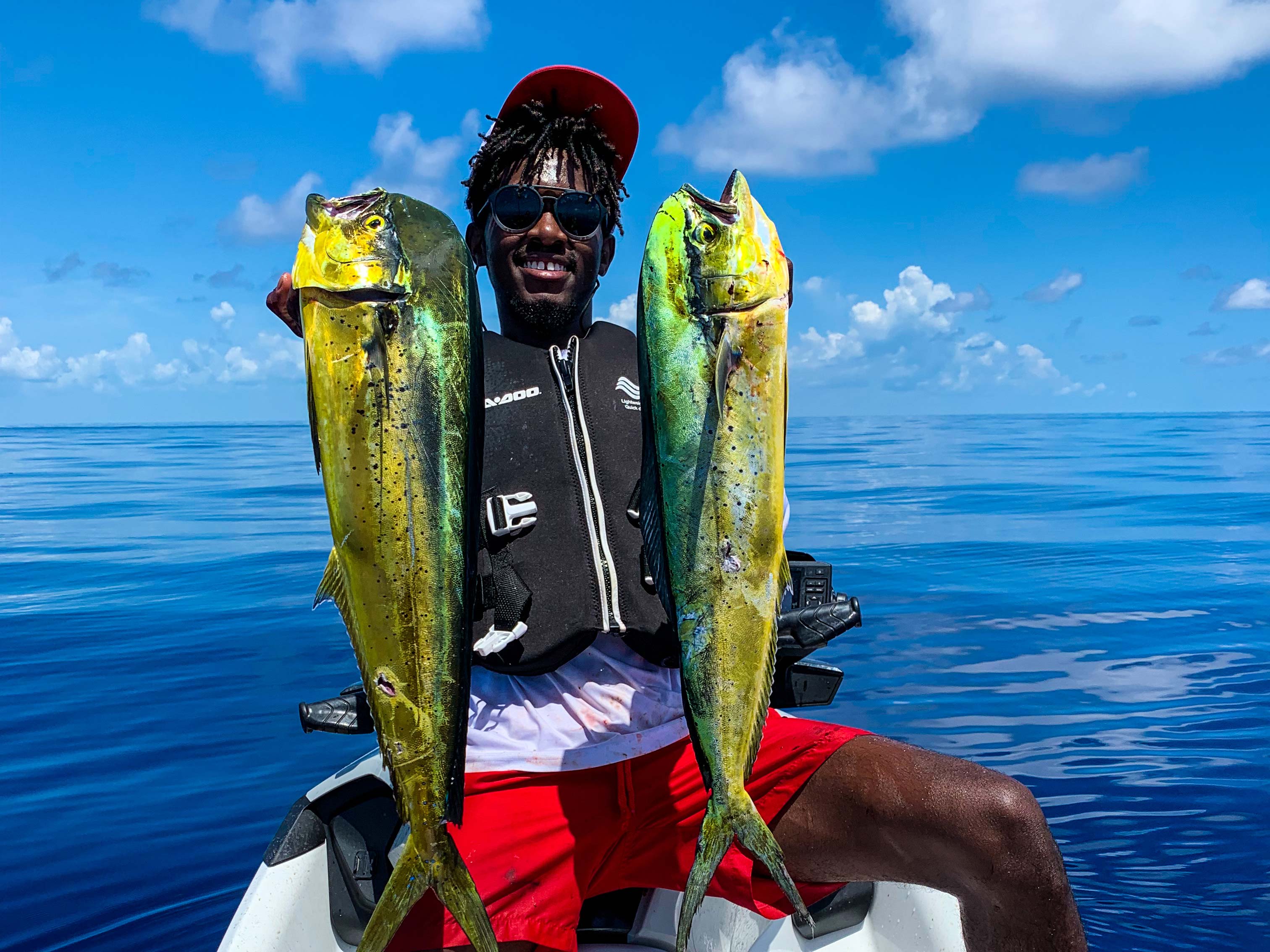 Emmanuel Williams holding two fishes on a Sea-Doo