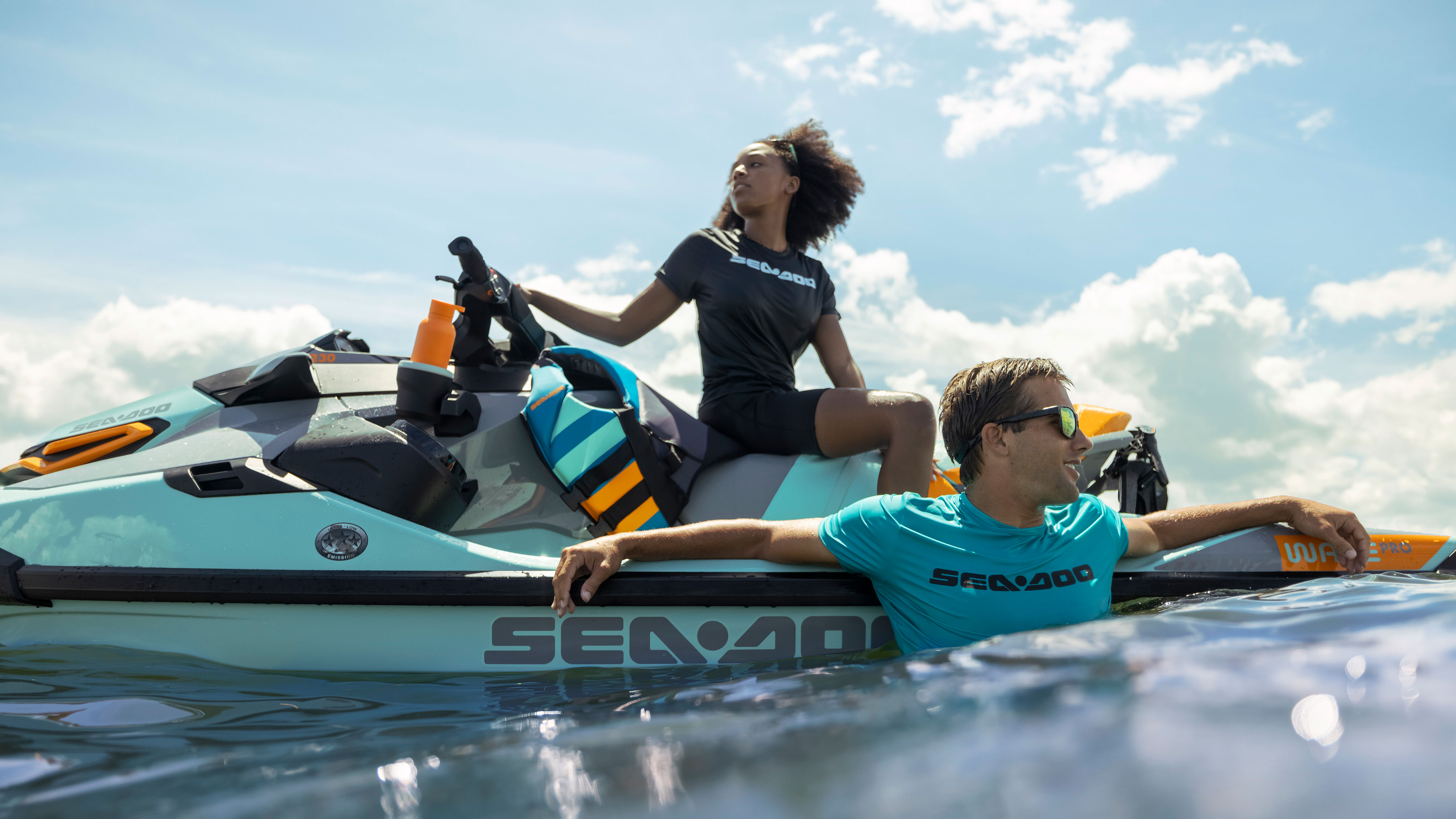 Woman sitting on a Sea-Doo Wake Pro with a man swimming next to her