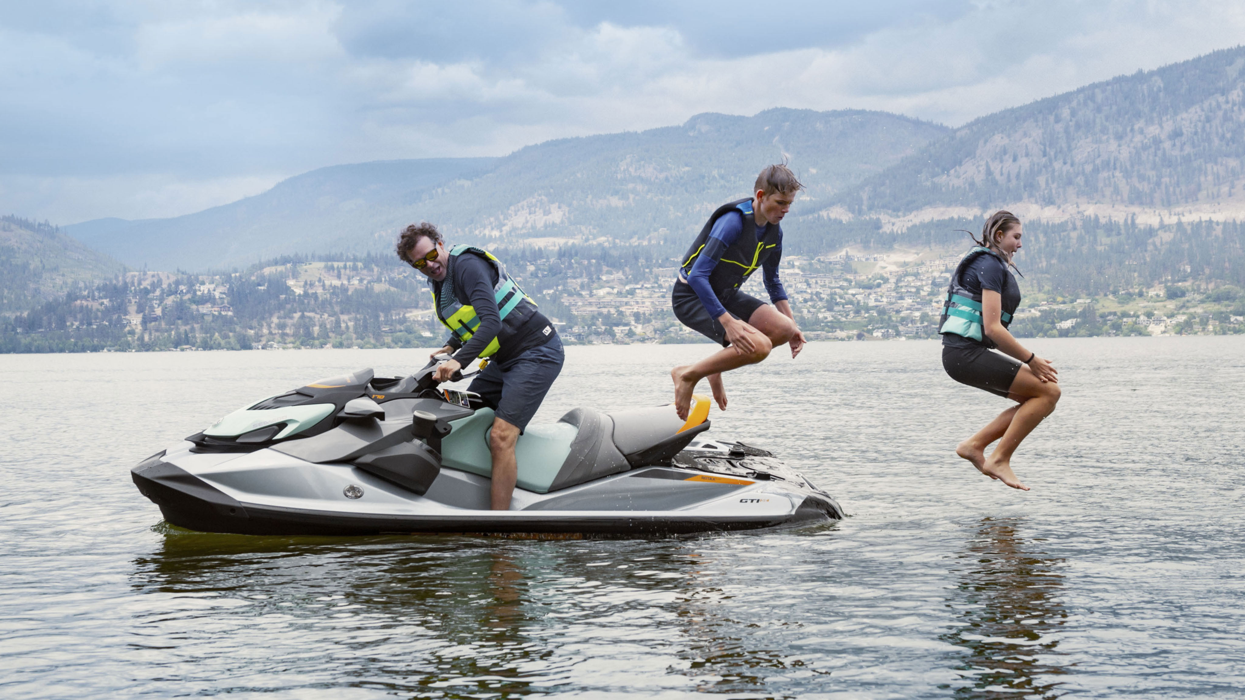 Een vader op een Sea-Doo GTI terwijl zijn twee kinderen in het water springen