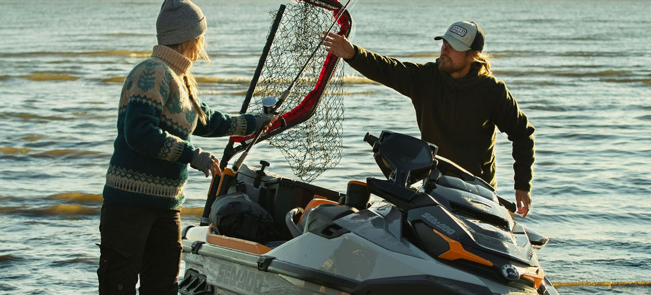 A couple loads their fish net and fishing rod into their Sea-Doo personal watercraft.